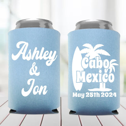 Two light blue can coolers with personalized text on a wooden surface.