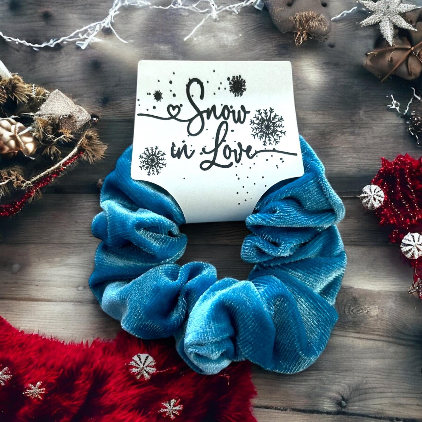 Blue scrunchies with a card reading 'Snow in Love' on a wooden surface with Christmas decorations.