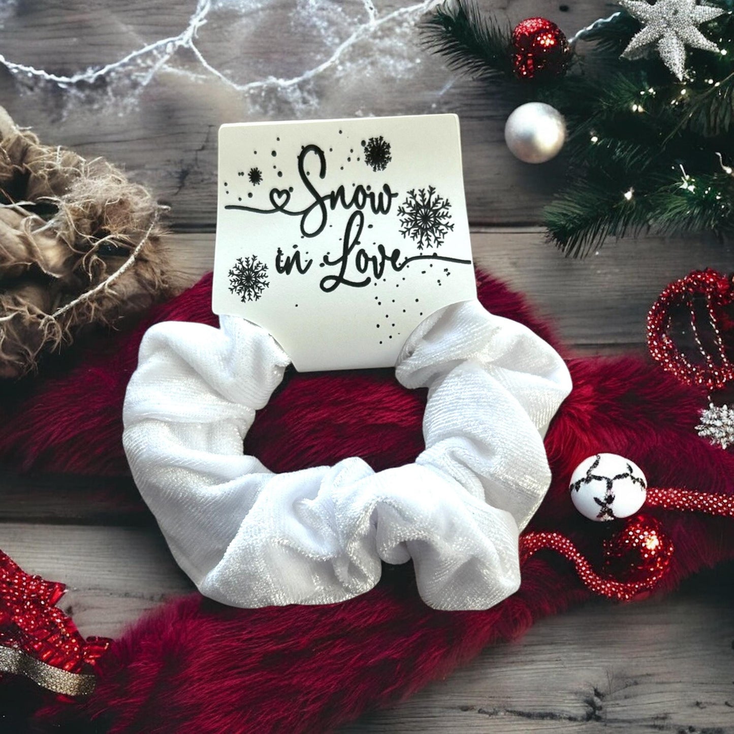 White scrunchie on a red fabric background with Christmas decorations and 'Snow in Love' card.