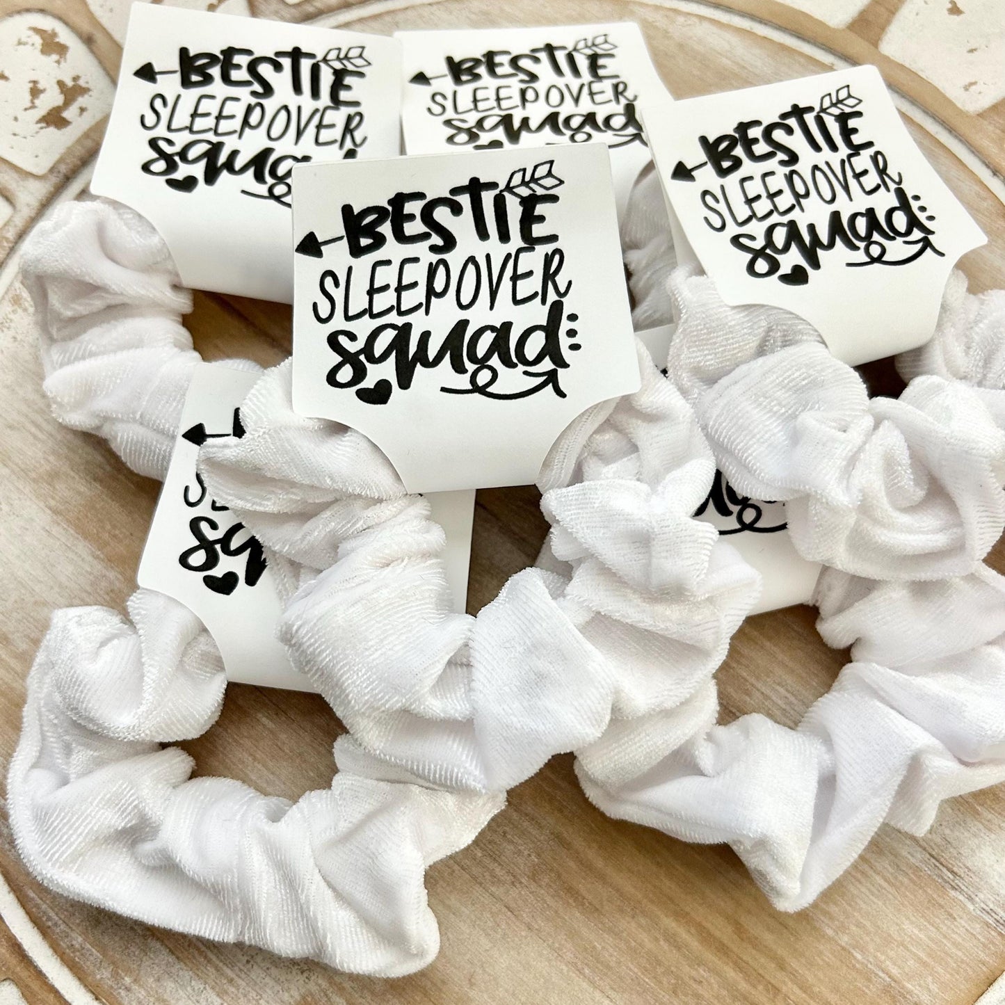 White scrunchies with 'Bestie Sleepover Squad' text on a wooden surface
