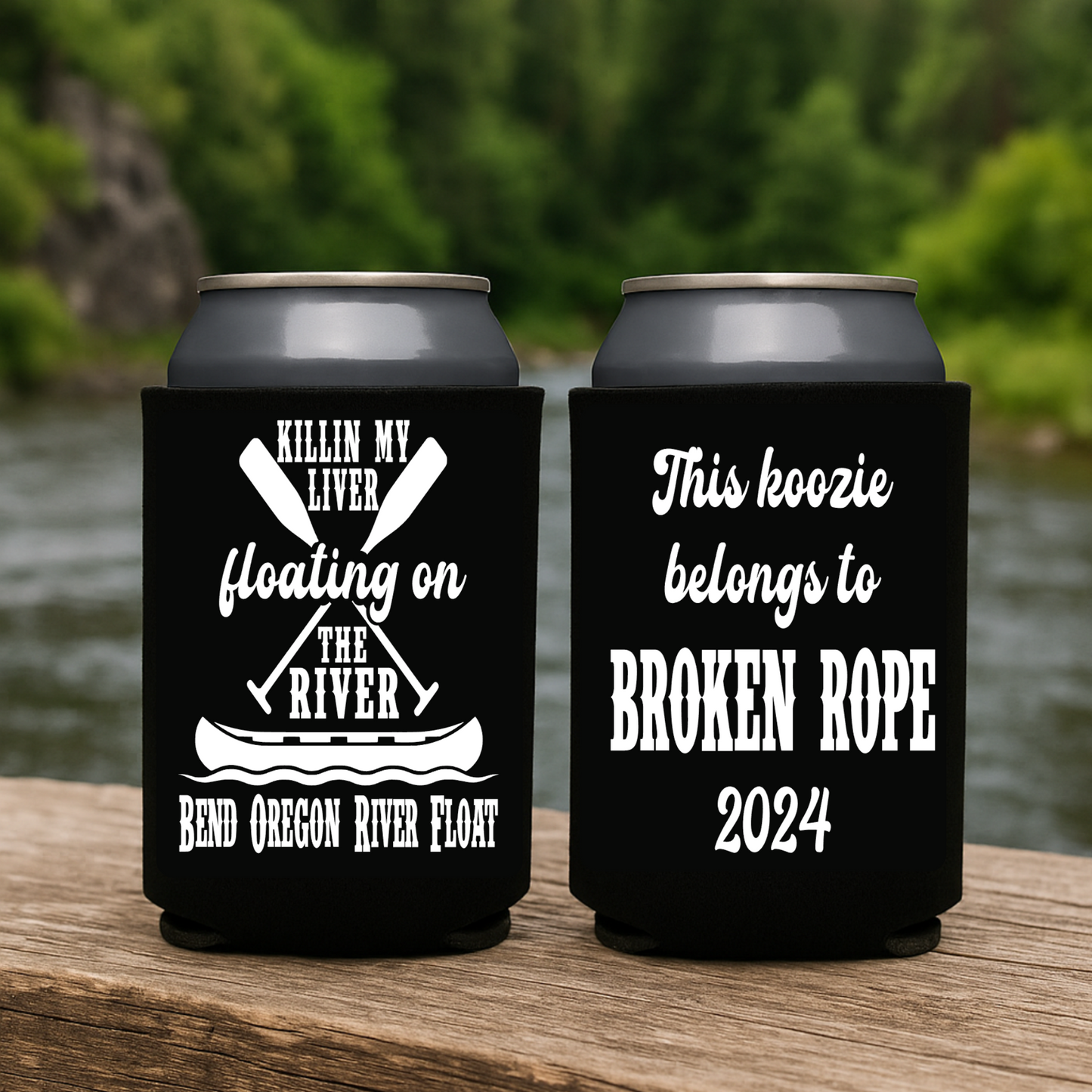 Two black can coolers with white text on a wooden surface by a river.