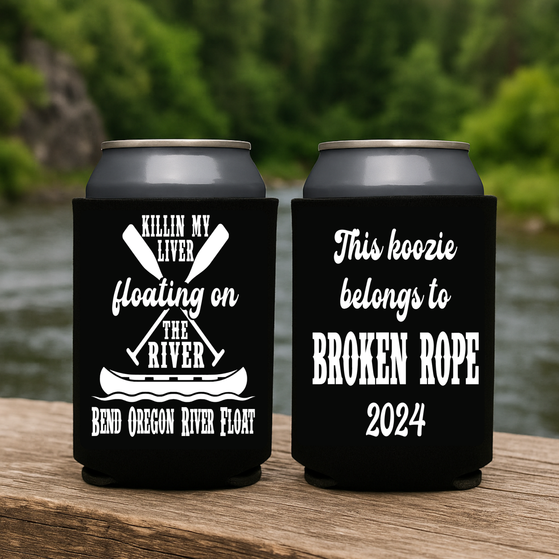 Two black can coolers with white text on a wooden surface by a river.