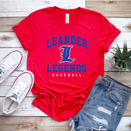 Red t-shirt with 'Leander Legends Baseball' text, white sneakers, and denim shorts on a wooden surface.
