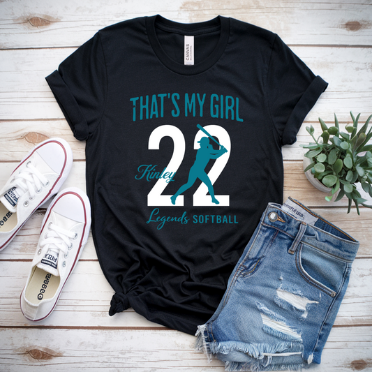 Black t-shirt with 'That's My Girl 22' design, white sneakers, denim shorts, and a plant on a wooden surface.