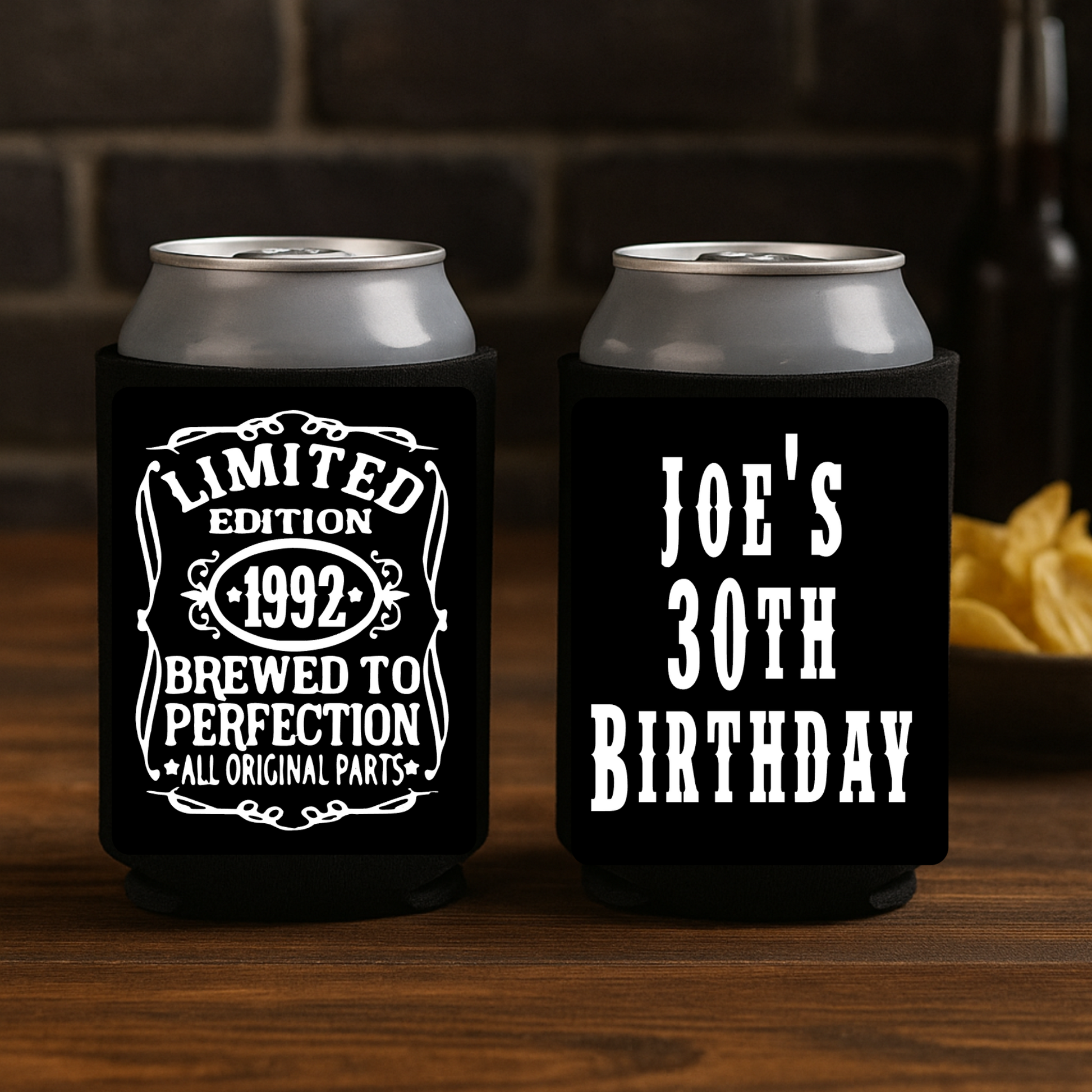 Two black can coolers with white text on a wooden surface.