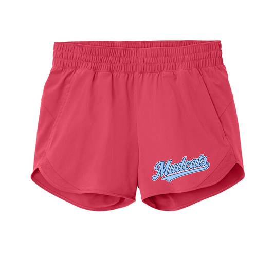 A pair of women's athletic shorts in a vibrant pinkish-red hue, featuring an elastic waistband and a light blue and white 'Mudcats' script logo on the lower left leg, shown against a plain white background.