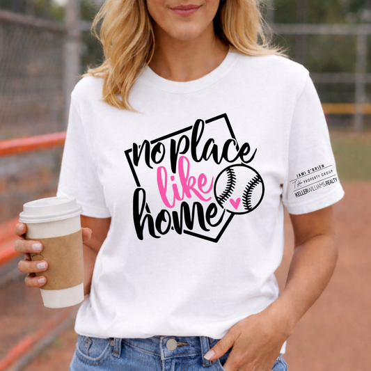 Woman wearing a white t-shirt with 'no place like home' and a baseball graphic, holding a coffee cup on a sports field.