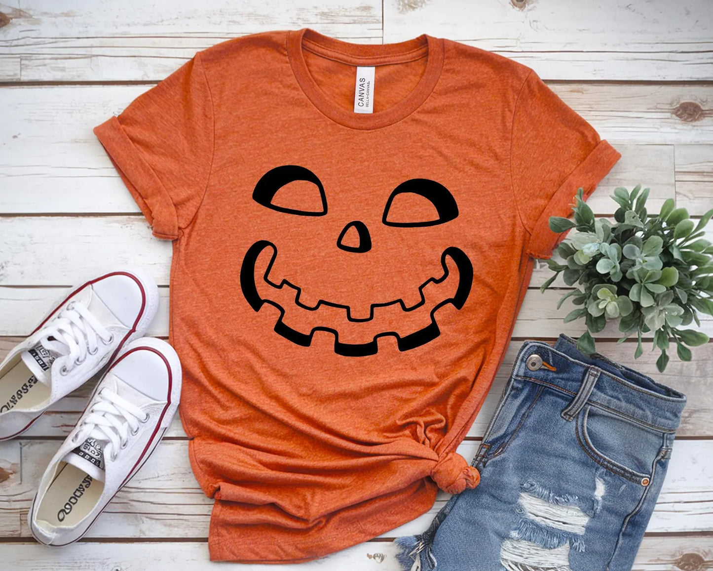 Orange t-shirt with a pumpkin face design, white sneakers, and blue jeans.