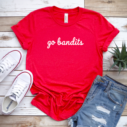 Red t-shirt with 'go bandits' text, white sneakers, and denim shorts on a wooden surface.