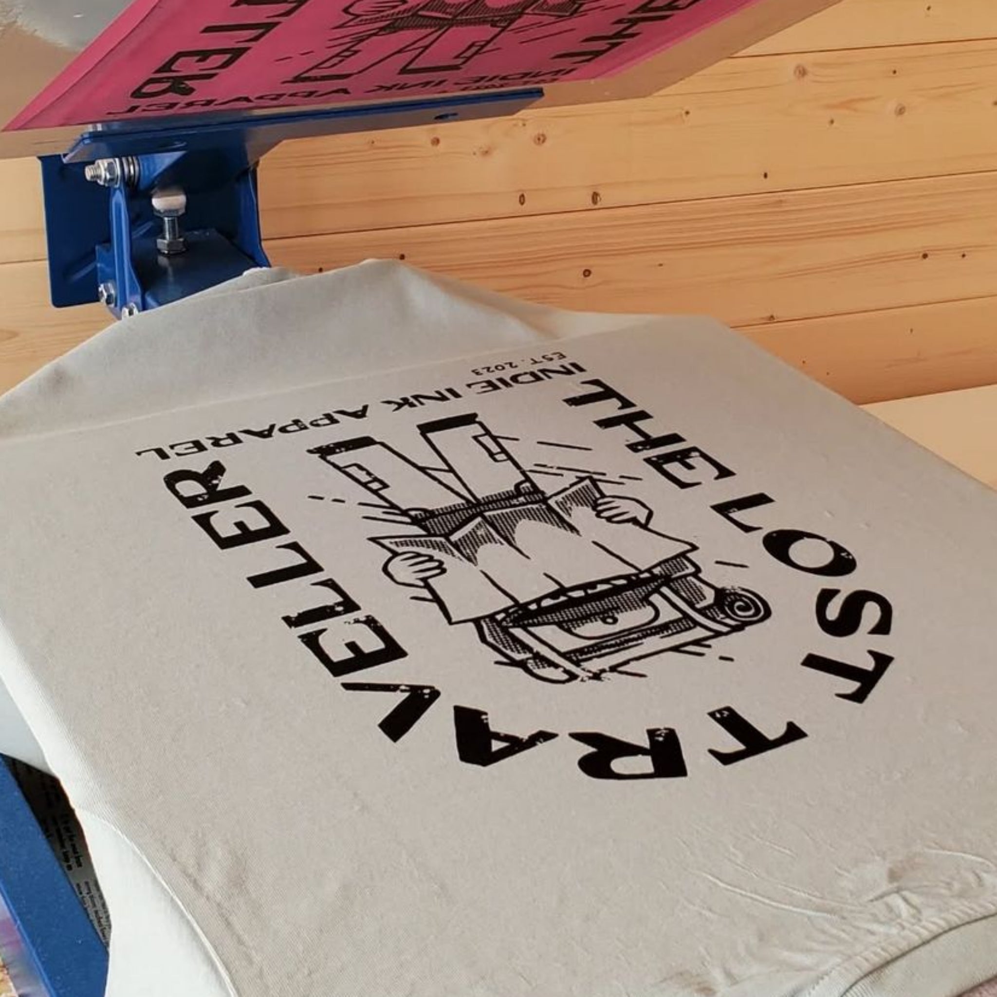 Screen printing process with a t-shirt and screen printing equipment on a wooden table.
