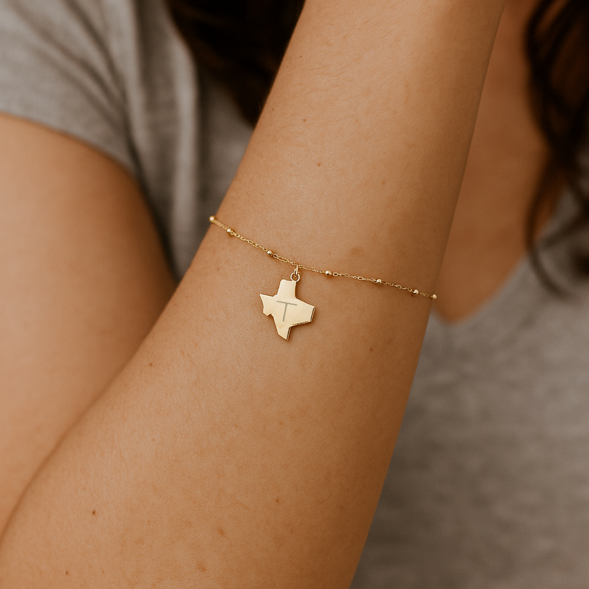 Gold bracelet with a Texas-shaped pendant on a person's wrist.